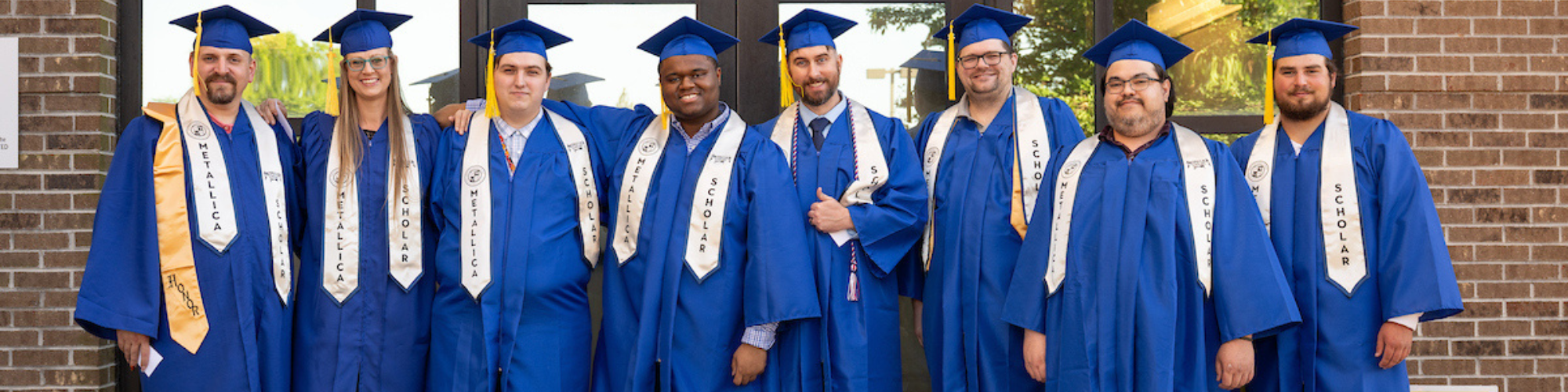 Group of graduates wearing blue caps and gowns and the Metallica Scholars stoles