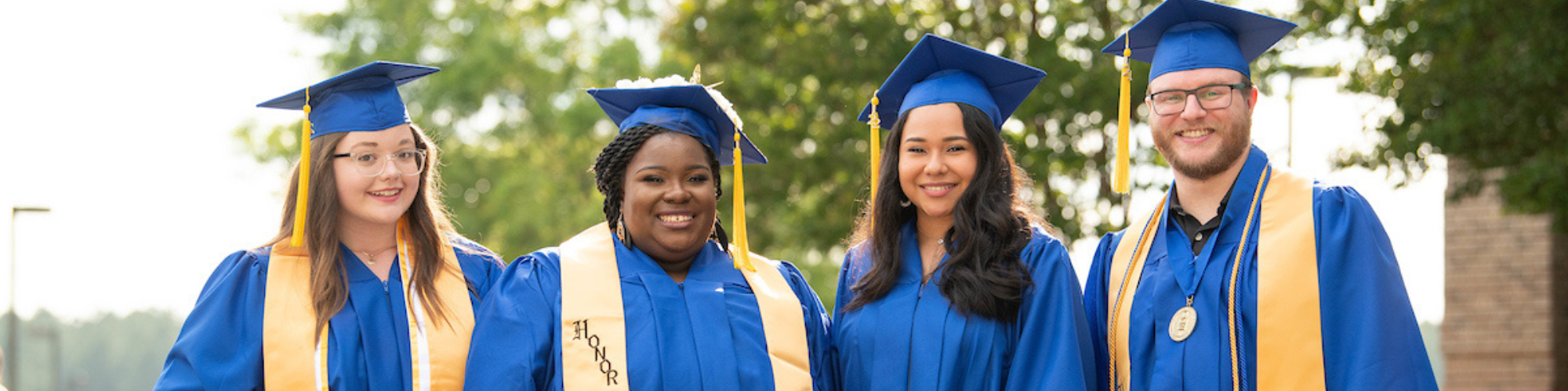 Three female graduates in cap and gown and one male graduate in cap and gown