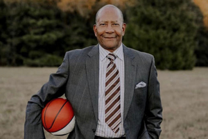 Black male dressed in grey suit holding a basketball