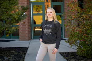 Female student wearing Aiken Technical College sweater and standing in front of building