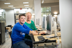 Student at computer receiving assistance from staff
